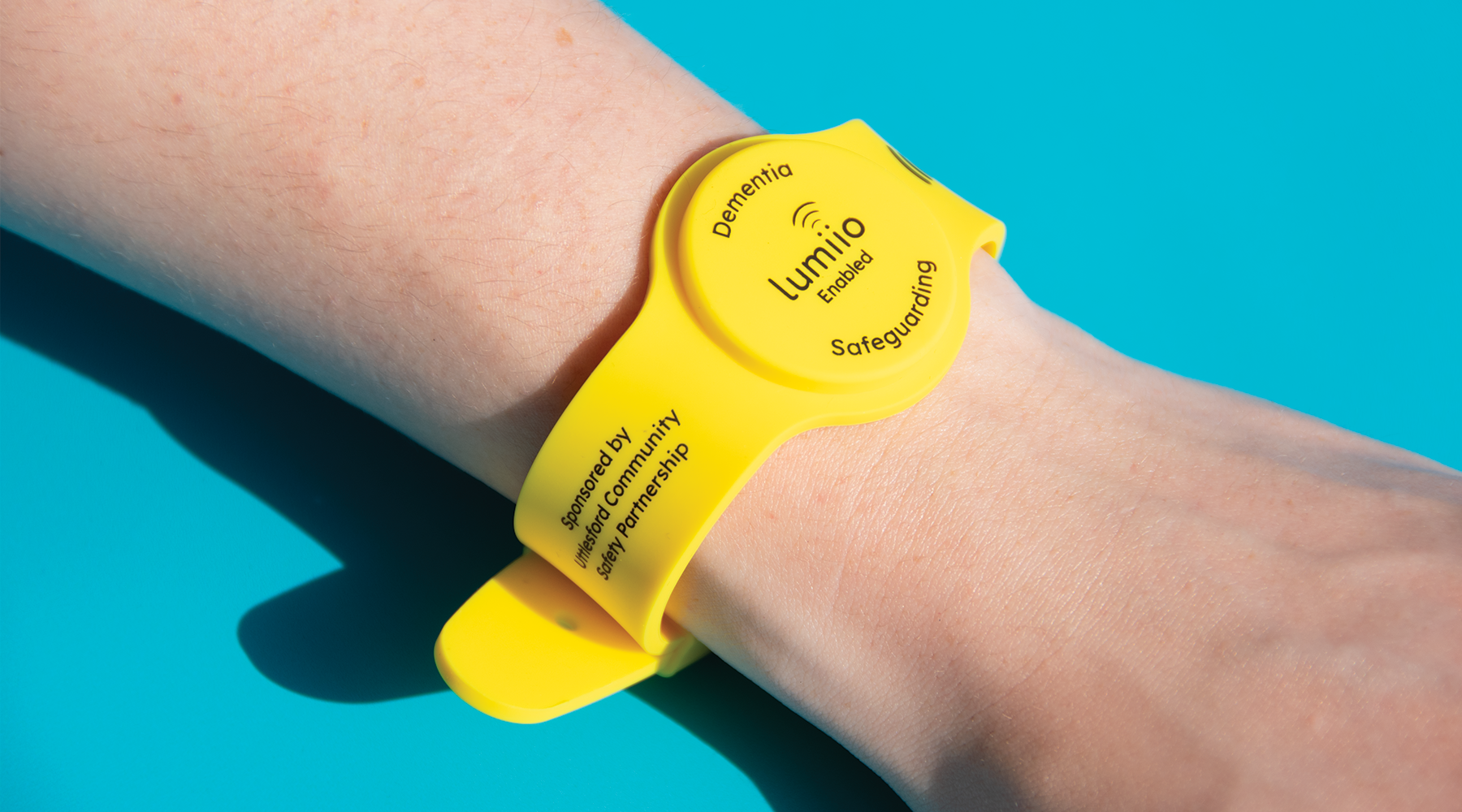 Yellow Uttlesford Dementia Wristband worn on a wrist against a blue background